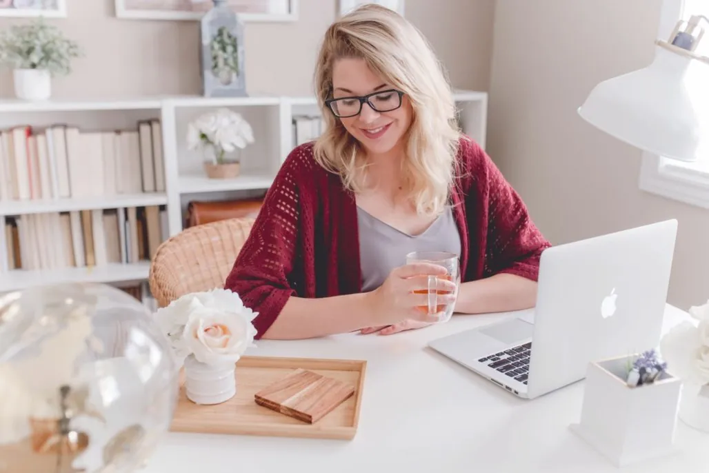 Remote work - blonde woman with glasses sitting in home office at desk while using Apple laptop