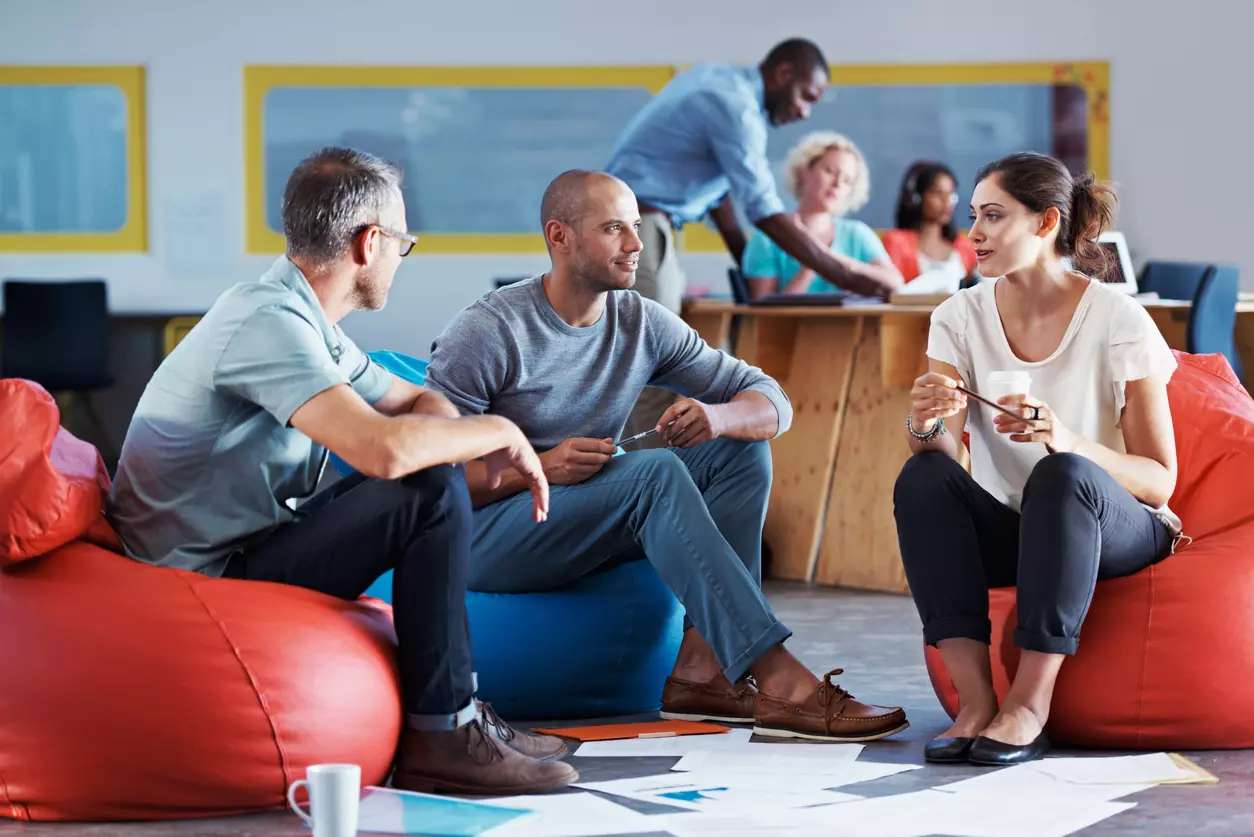 Internal communication - two male employees and a female employee sitting on beanbag chairs and discussing a project