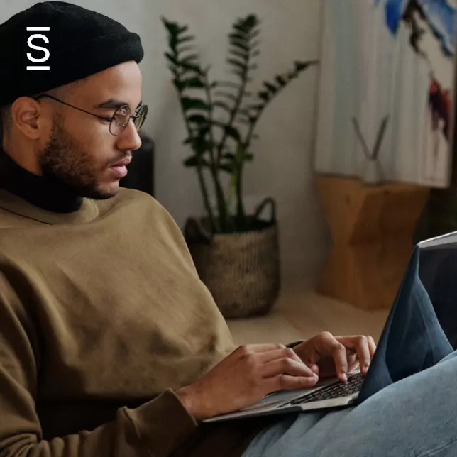 Remote work tools - man wearing glasses and beanie using laptop computer while working at home