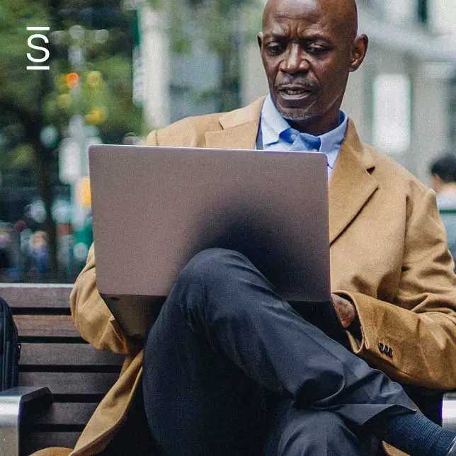 Digital workplace - man sitting on park bench and working on laptop computer