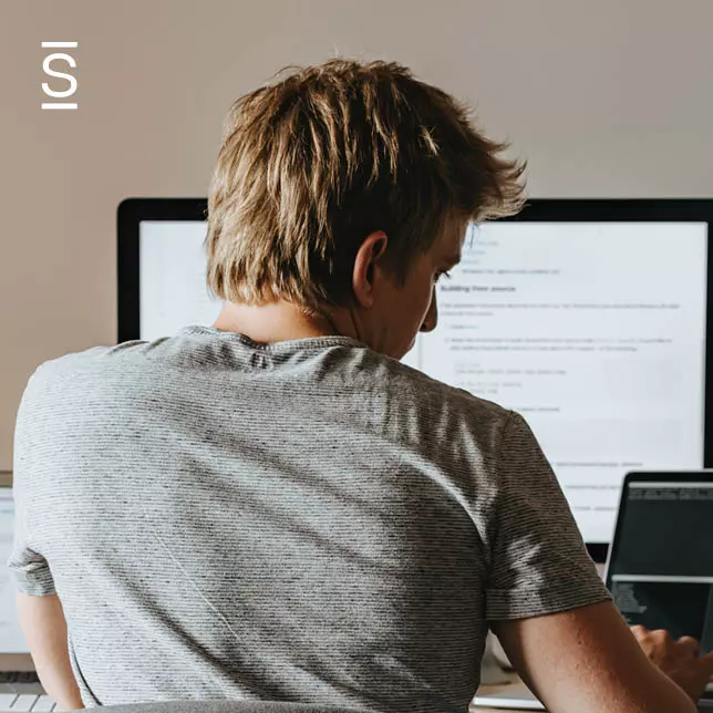 Work From Home - man in grey shirt using laptop and desktop at the same time