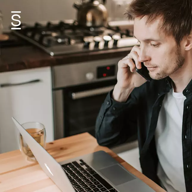 Remote work - man working in his kitchen on laptop while speaking on smartphone