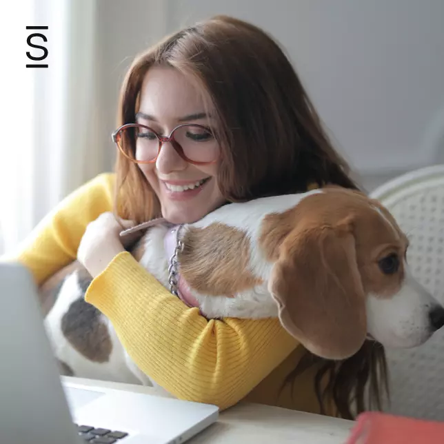 Employees - woman with glasses smiling and holding her beagle while looking at laptop