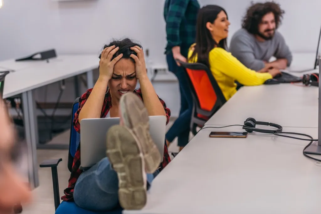 Poor employee experience - A nervous female office worker with her legs on her desk and her laptop in her lap having a hard day.